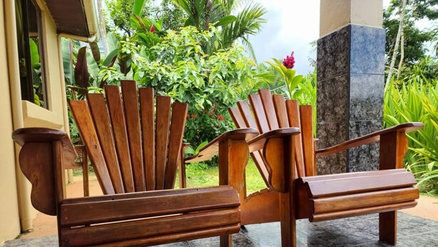 A wooden bench with a backrest and armrests, placed on a tiled floor. - Ceibo Arenal Home (La Fortuna)