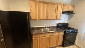 A kitchen with wooden cabinets, a black refrigerator, a sink, and a stove. - Starlite Motel (Stanton)