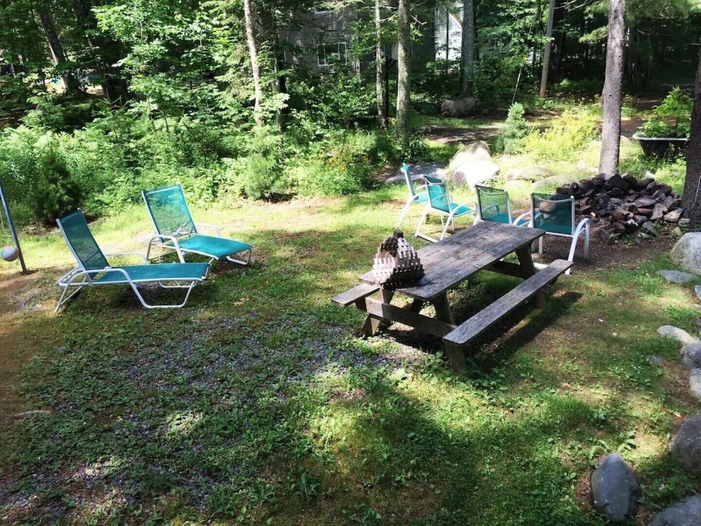 An outdoor seating area with a wooden picnic table and four green lawn chairs.
