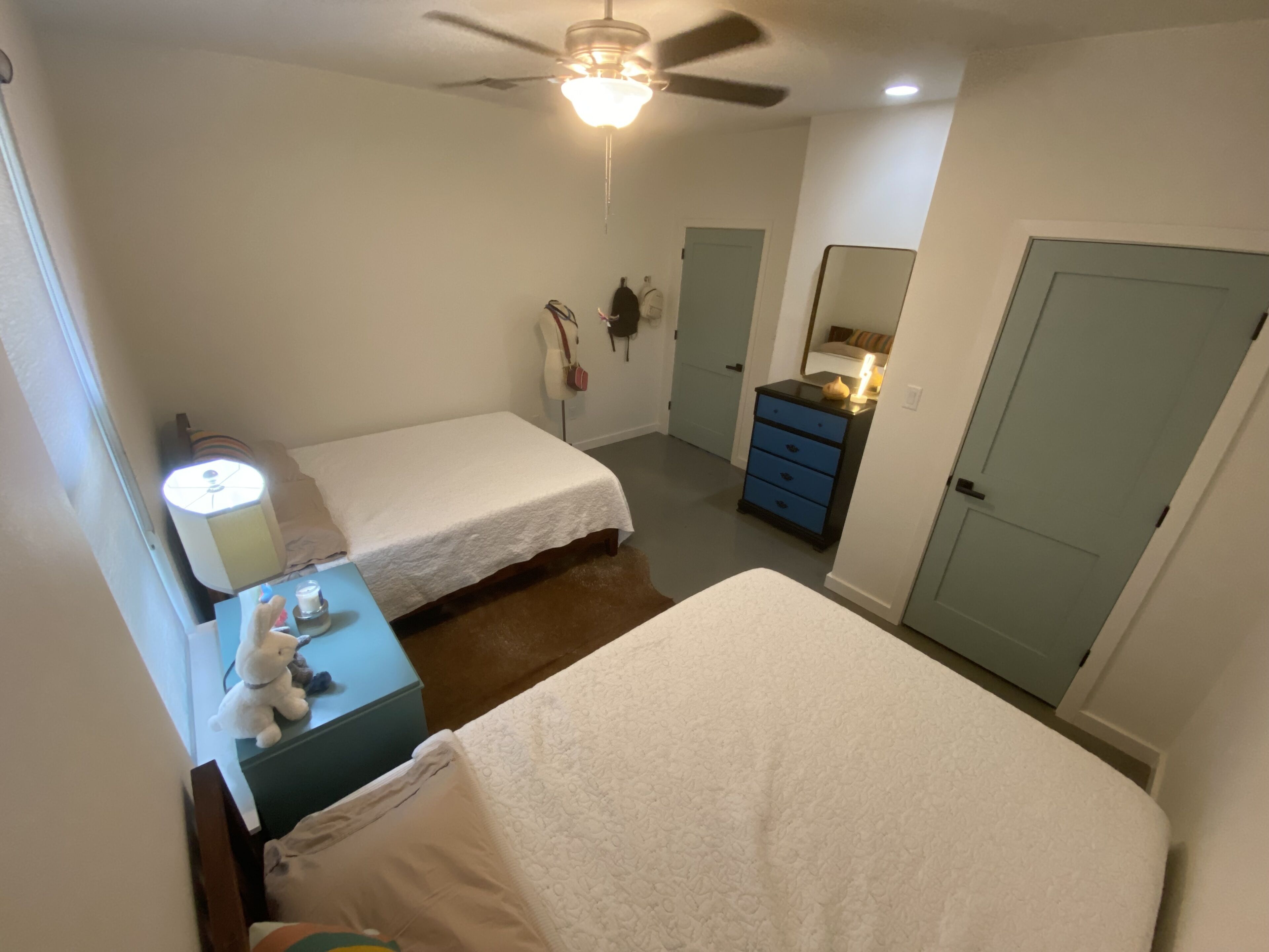 Un dormitorio con dos camas, un tocador, un espejo y un ventilador de techo.