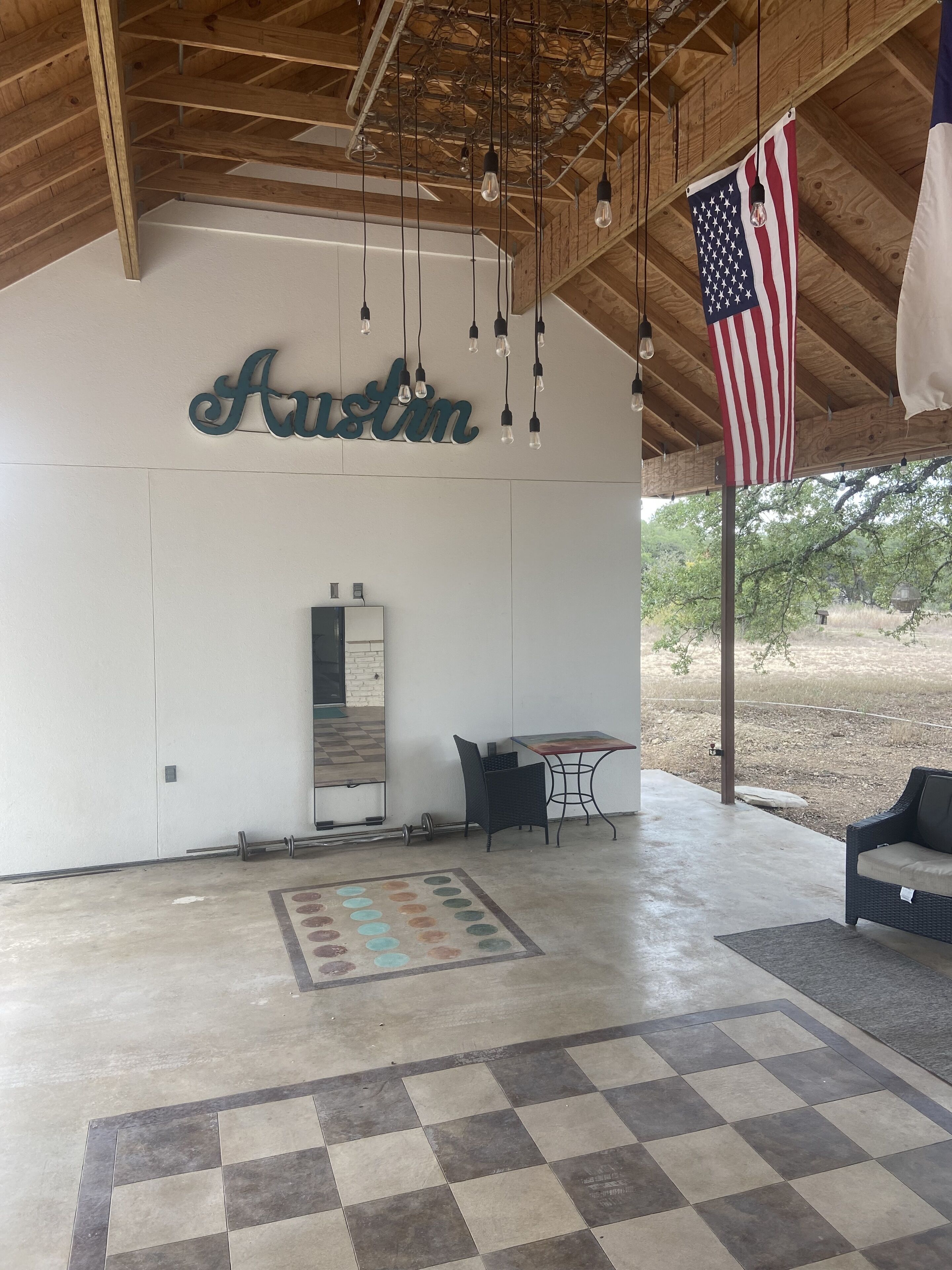A spacious indoor area with a wooden ceiling, a wall-mounted sign reading "Austin," a table with chairs, and an American flag.