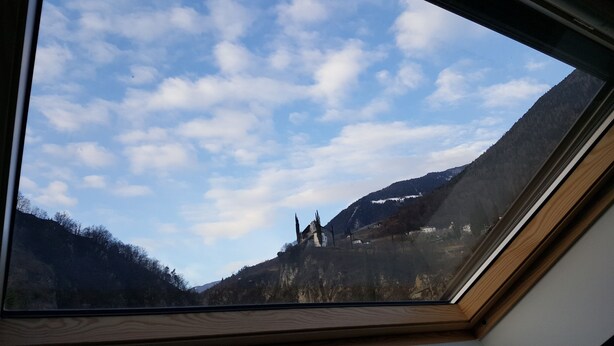 A view through a skylight of a mountainous landscape with a castle-like structure. - Above the roofs of Lana - Green Apartment - via Dolce Vita (Lana)