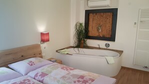 A bedroom with a bed, a nightstand, a red lamp, a wooden-framed mirror, a potted plant, and a bathtub. - Above the roofs of Lana - Green Apartment - via Dolce Vita (Lana)