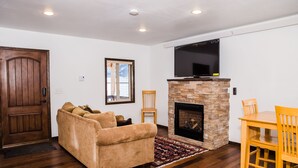 Una sala de estar con chimenea, un sofá, una mesa de comedor con sillas y un televisor sobre la chimenea.