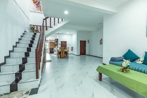 A spacious living area with a marble staircase, a green sofa with cushions, and a dining area with a table and chairs.