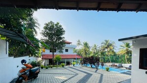 A covered outdoor area with a tiled floor, a parked scooter, a swimming pool, and a building with a red roof. - Villa Talpe 5 Bedrooms & Massage Pool (Unawatuna)