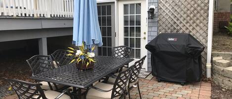 A patio with a table and chairs, a barbecue grill, and a decorative flower arrangement.