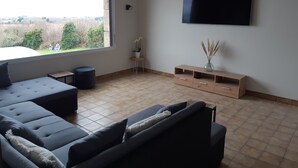 Uma sala de estar moderna com uma janela grande, uma TV de tela plana, um móvel de madeira para TV e um sofá seccional.