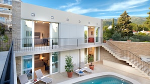Ein modernes, zweistöckiges Gebäude mit Pool, Sitzgelegenheiten im Freien und einer Treppe, die zu einem Balkon führt.