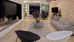 Ein modernes Wohnzimmer mit Flachbildfernseher, einer Couch, zwei Sesseln, einem Couchtisch und einem Kamin.