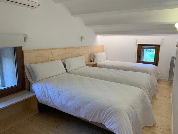 Quarto com duas camas, cabeceiras de madeira, roupa de cama branca, uma janela pequena e um radiador.