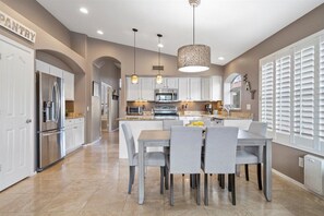 A modern kitchen with white cabinets, a central island, and a dining area with grey chairs. - Luxe Arizona Retreat...Family-Friendly Home (Phoenix)