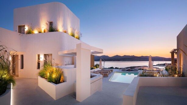 A modern outdoor pool area with a view of the sea and mountains at sunset. - White Pebble Suites (Milos)