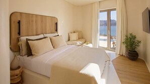 A bedroom with a large bed, a wooden headboard, a small table with a plant, and a view of the sea through a sliding door. - White Pebble Suites (Milos)