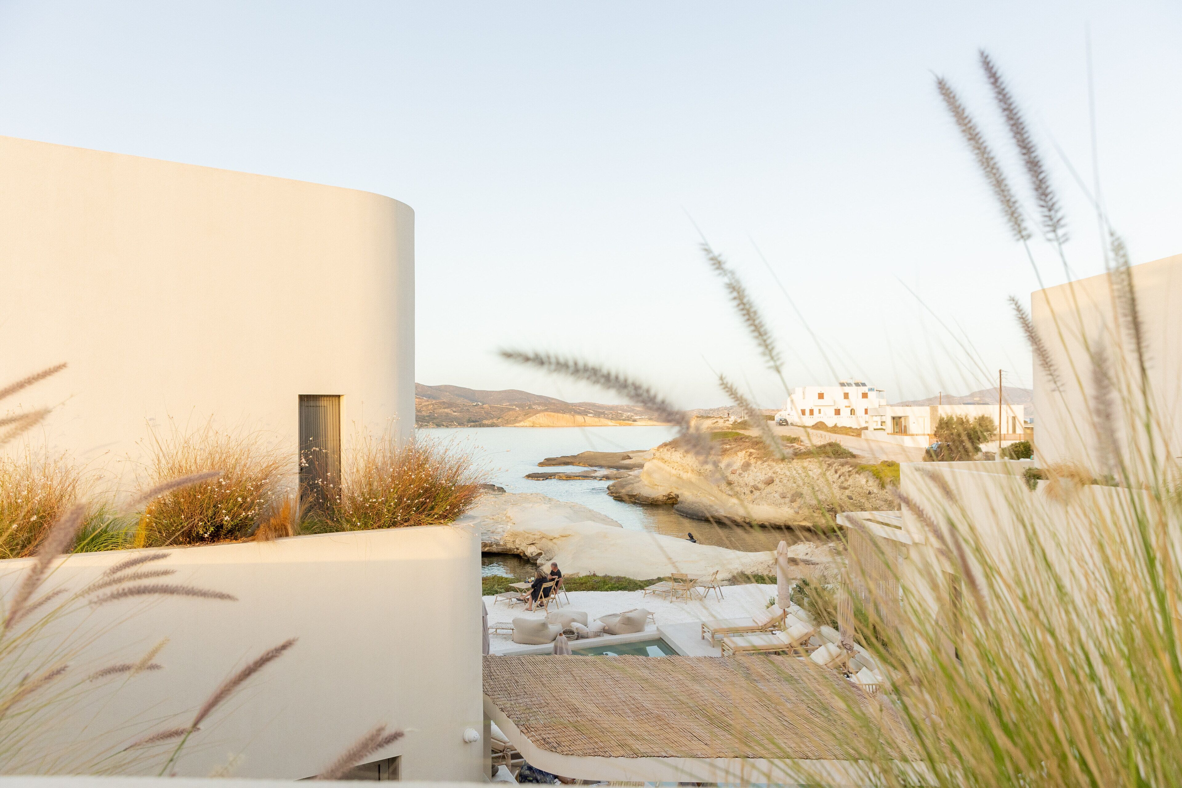 A modern building with a pool area, outdoor seating, and a view of the sea.
