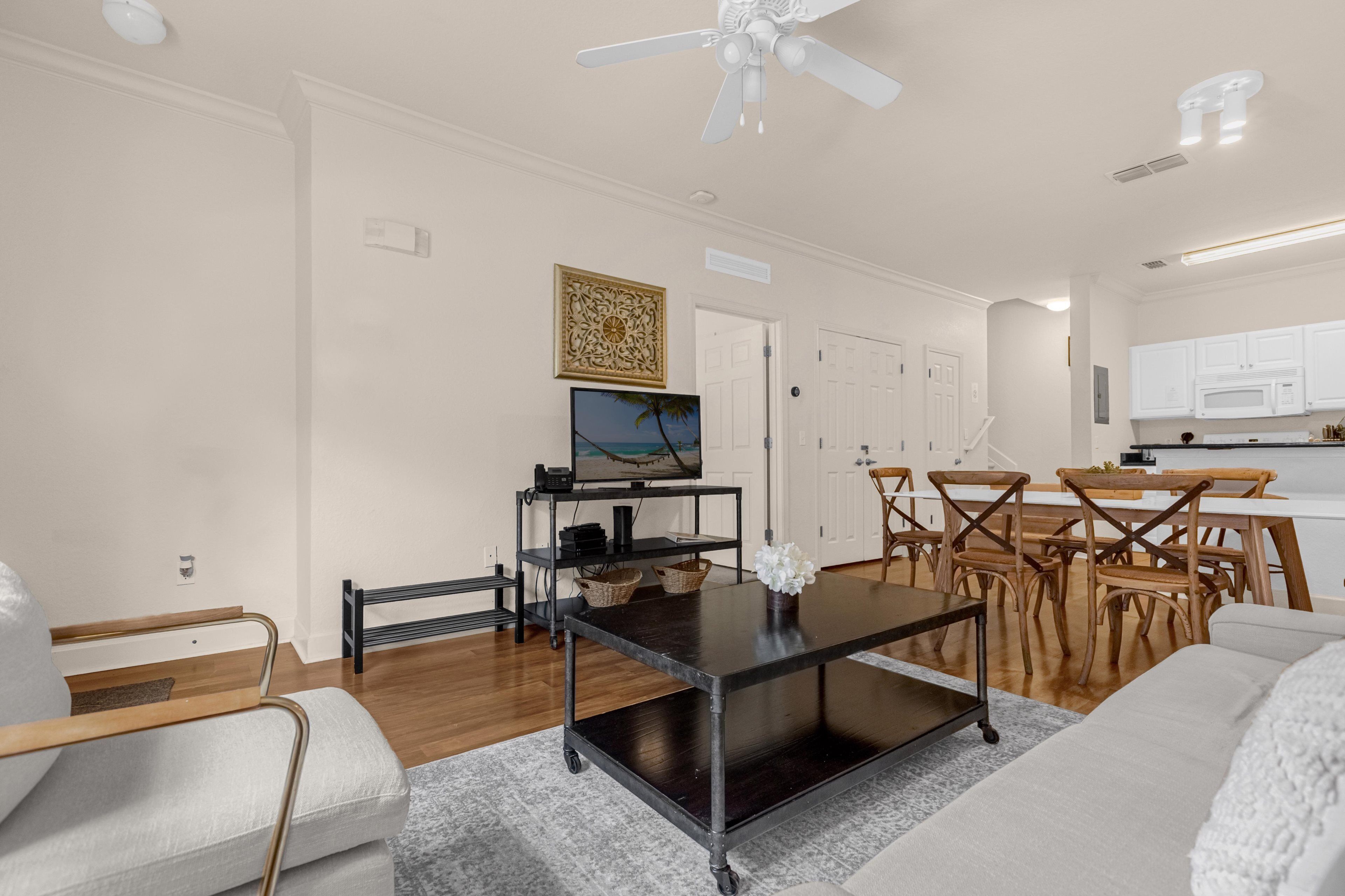 Una sala de estar moderna con un sofá, una mesa de centro, un televisor y un comedor con sillas y mesa de madera.