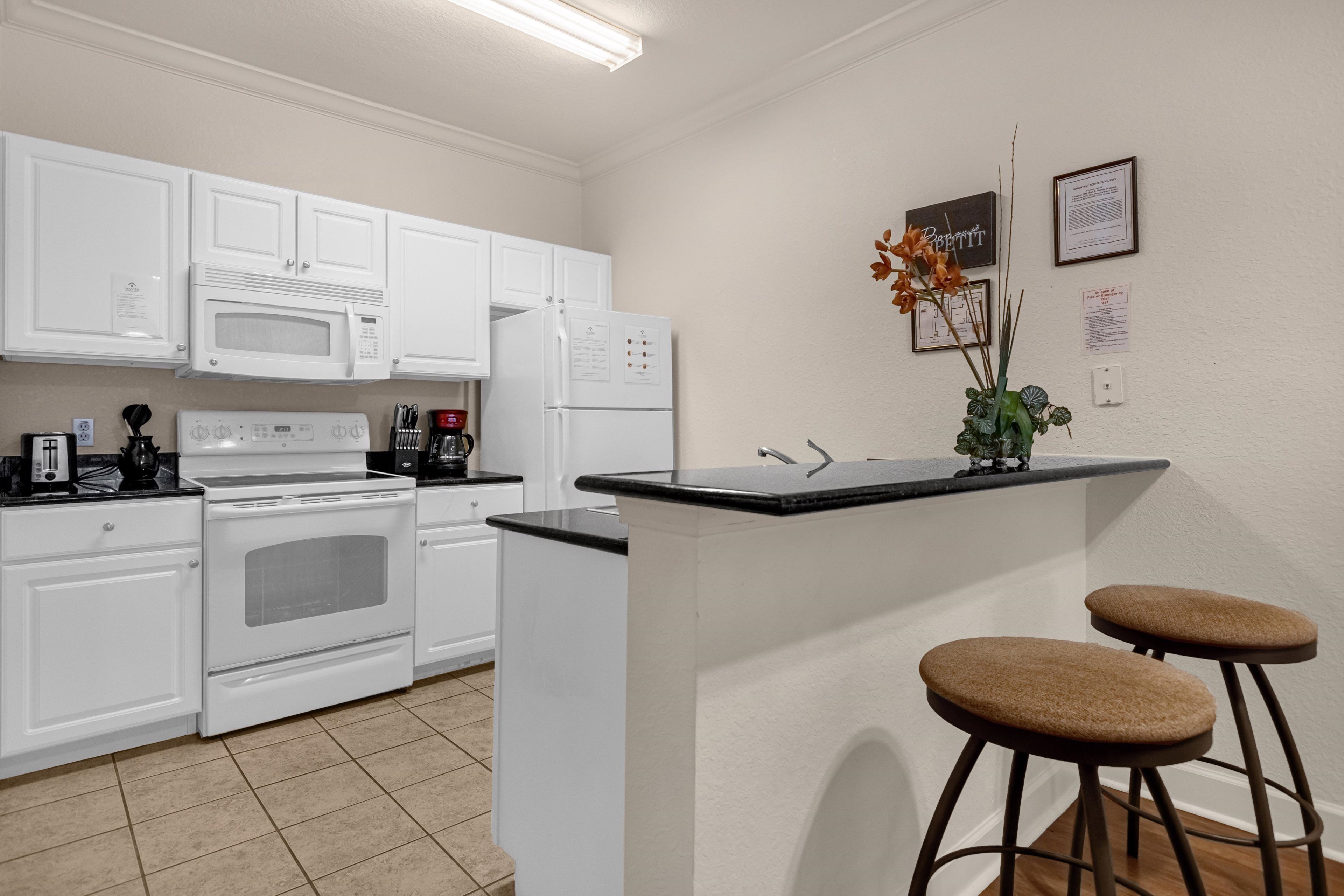 Une cuisine moderne avec des meubles blancs, un four à micro-ondes, une cuisinière, un réfrigérateur et un petit coin bar avec des tabourets.