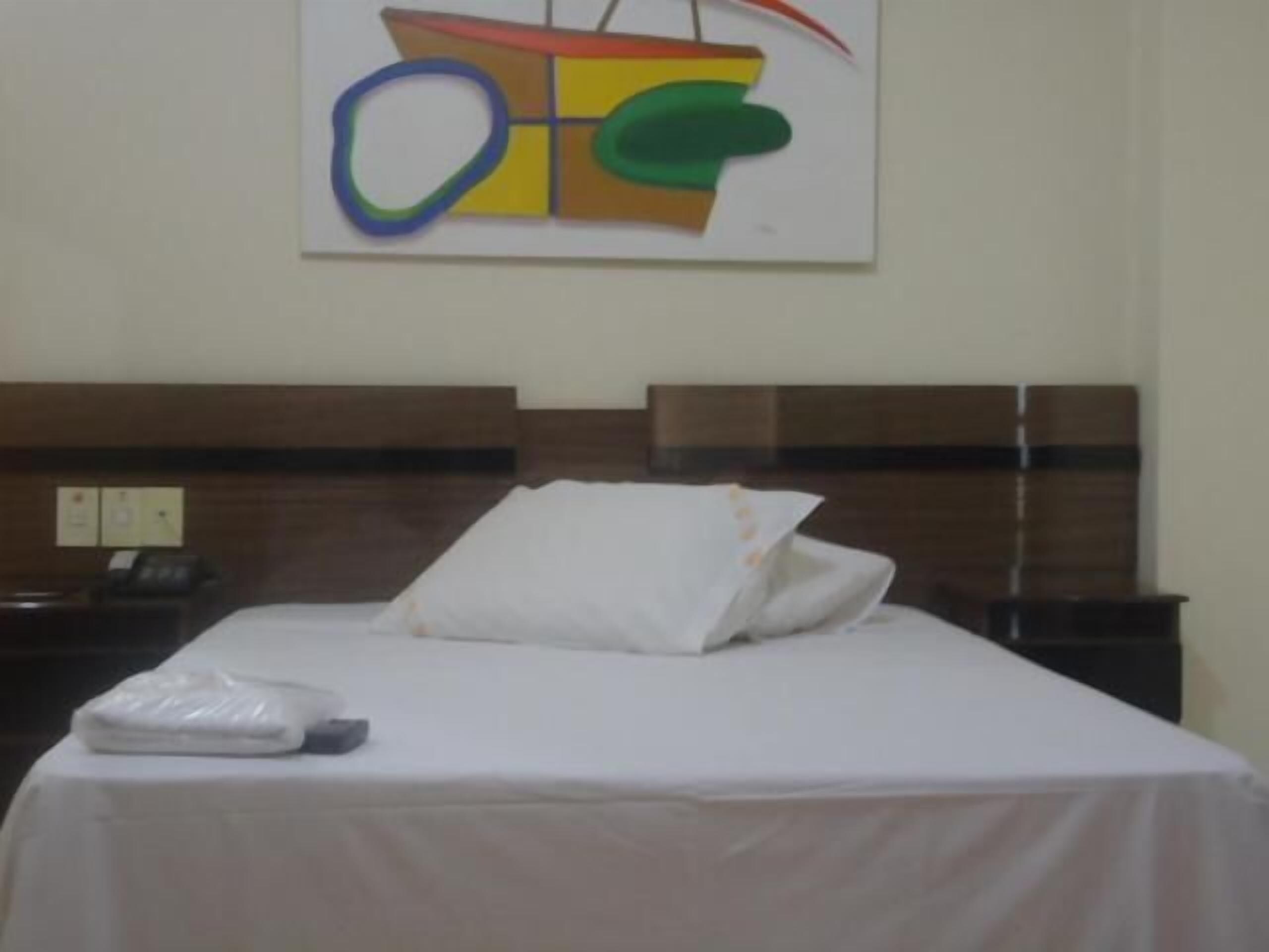 Een hotelkamer met een bed, nachtkastje en een schilderij aan de muur.