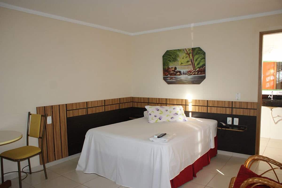 Une chambre d’hôtel avec un lit, une chaise, une petite table, un tableau au mur et une vue sur l’extérieur.