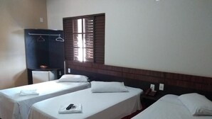 A hotel room with three single beds, a wardrobe, a window with blinds, and a small table with a phone and a bottle. - Hotel Colorado (Rio Verde)