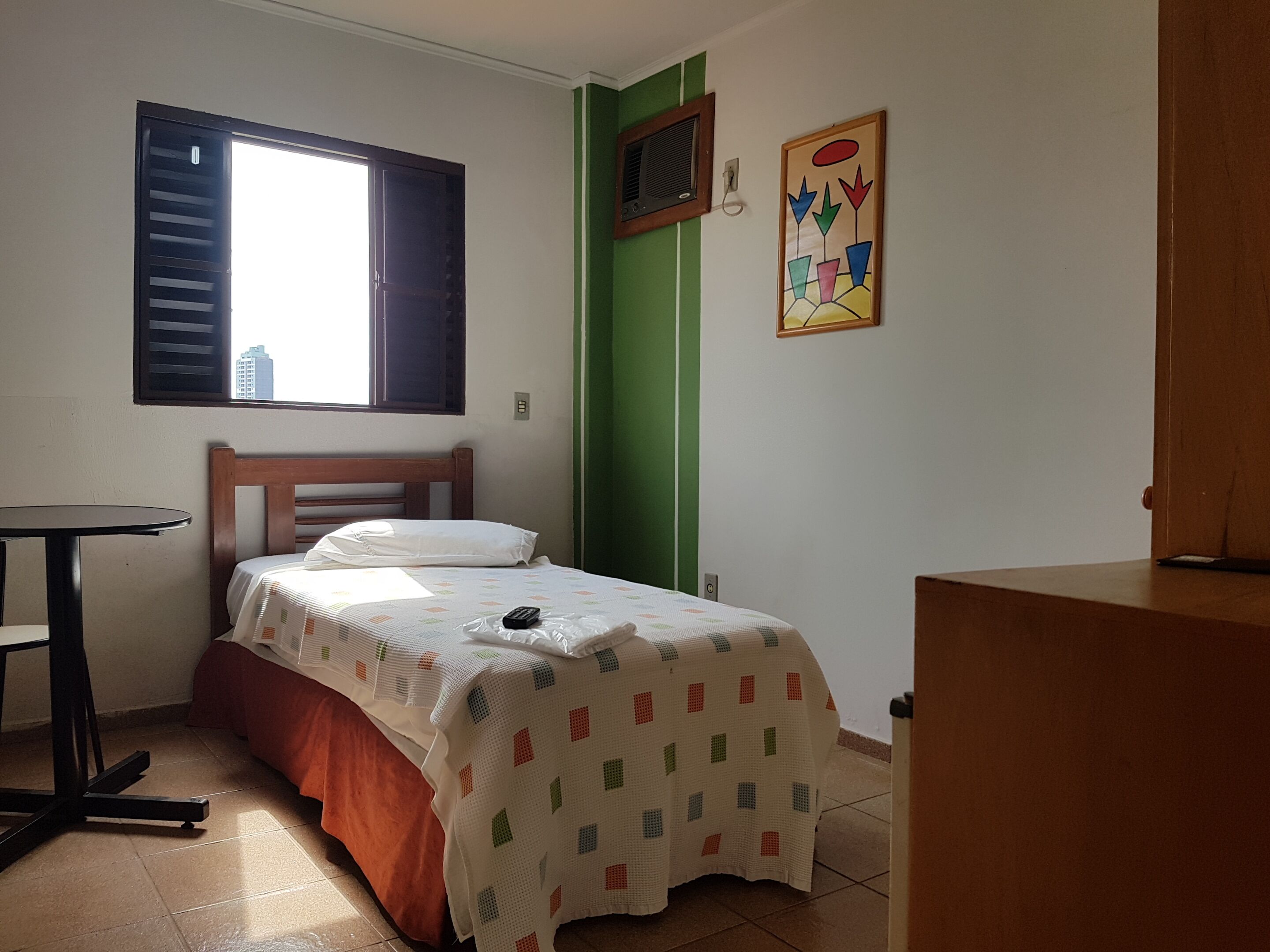 A small, neatly arranged bedroom with a bed, a small table, and a window.