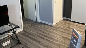 Un espacio habitable compacto con kitchenette, una puerta que conduce a otra habitación, una alfombra pequeña y un calentador.