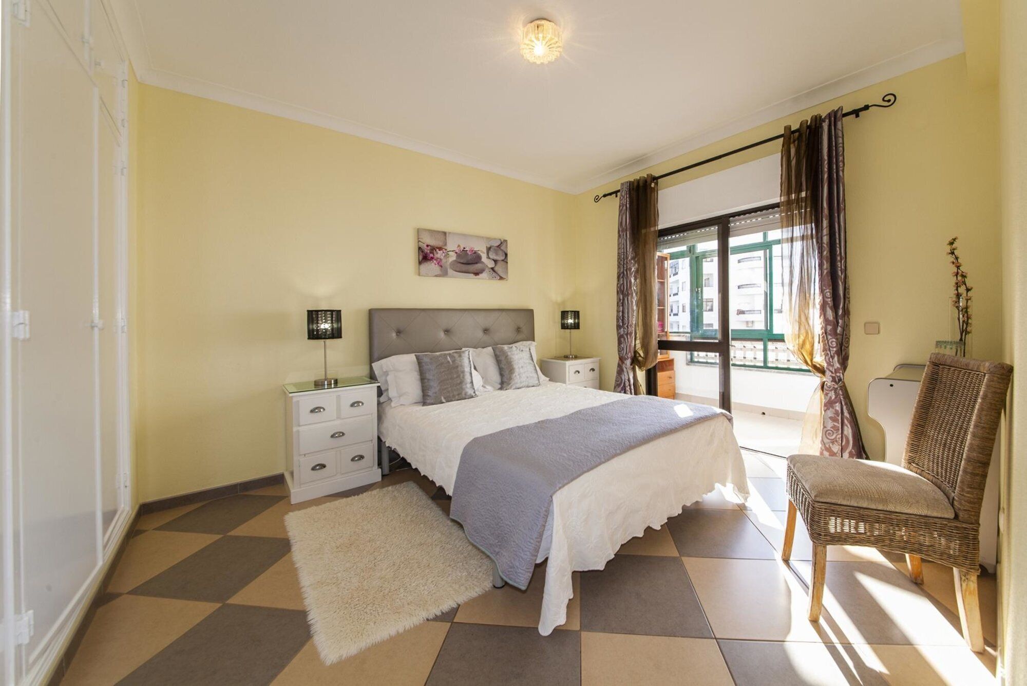 A bedroom with a bed, nightstands, a chair, a window with curtains, and a painting on the wall.