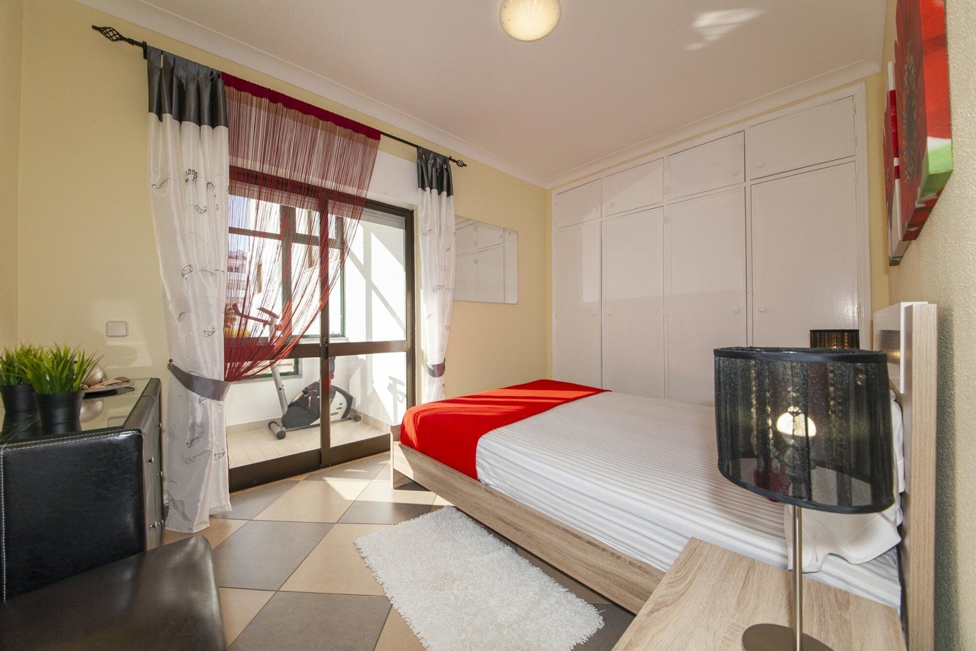 A bedroom with a bed, a desk, a chair, a lamp, and a window with curtains.