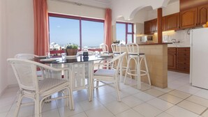 Una cocina moderna con armarios blancos, un comedor con sillas de mimbre y vistas al mar a través de amplias ventanas.
