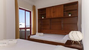 Una habitación de hotel con una cama, cabecera de madera, una mesita con lámpara y vista a la ciudad por la ventana.