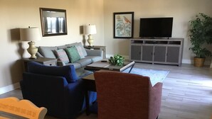 Una sala de estar con un sofá, dos sillones, una mesita de centro, un televisor y un mueble.