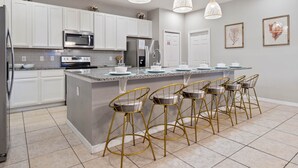 A modern kitchen with white cabinets, stainless steel appliances, a granite countertop, and gold bar stools. - Waterpark, Caribbean Backyard, Epic Game Room w/ Pool Table: Florida Dreamin (Davenport)