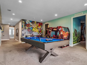 A pool table in a room with a colorful mural and arcade games.
