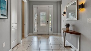 Un couloir avec des portes blanches, une console sur laquelle est posée une plante, et un miroir fixé au mur.