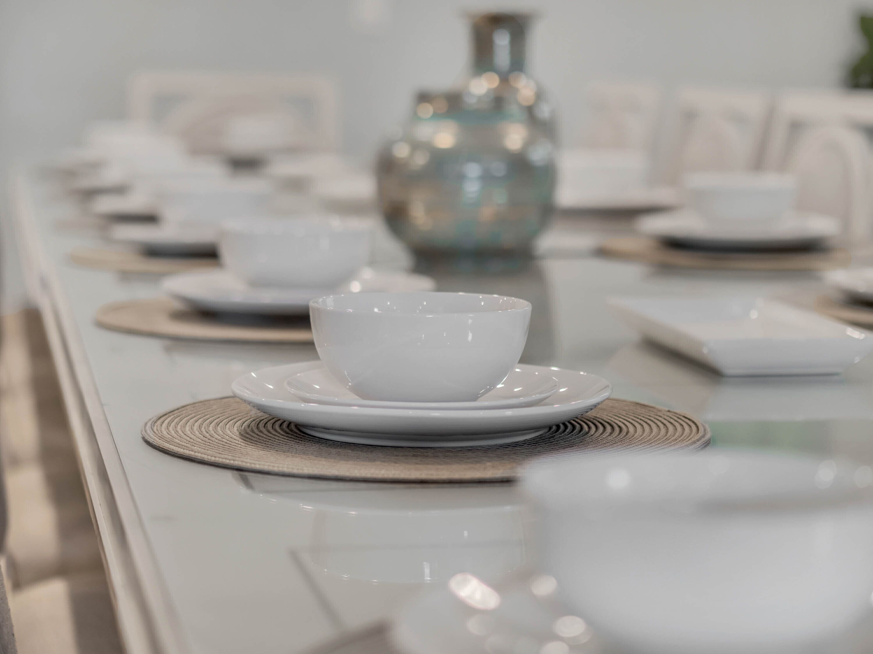 A dining table set with white bowls and plates, a decorative vase, and a woven placemat.