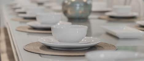 A dining table set with white bowls and plates, a decorative vase, and a woven placemat.