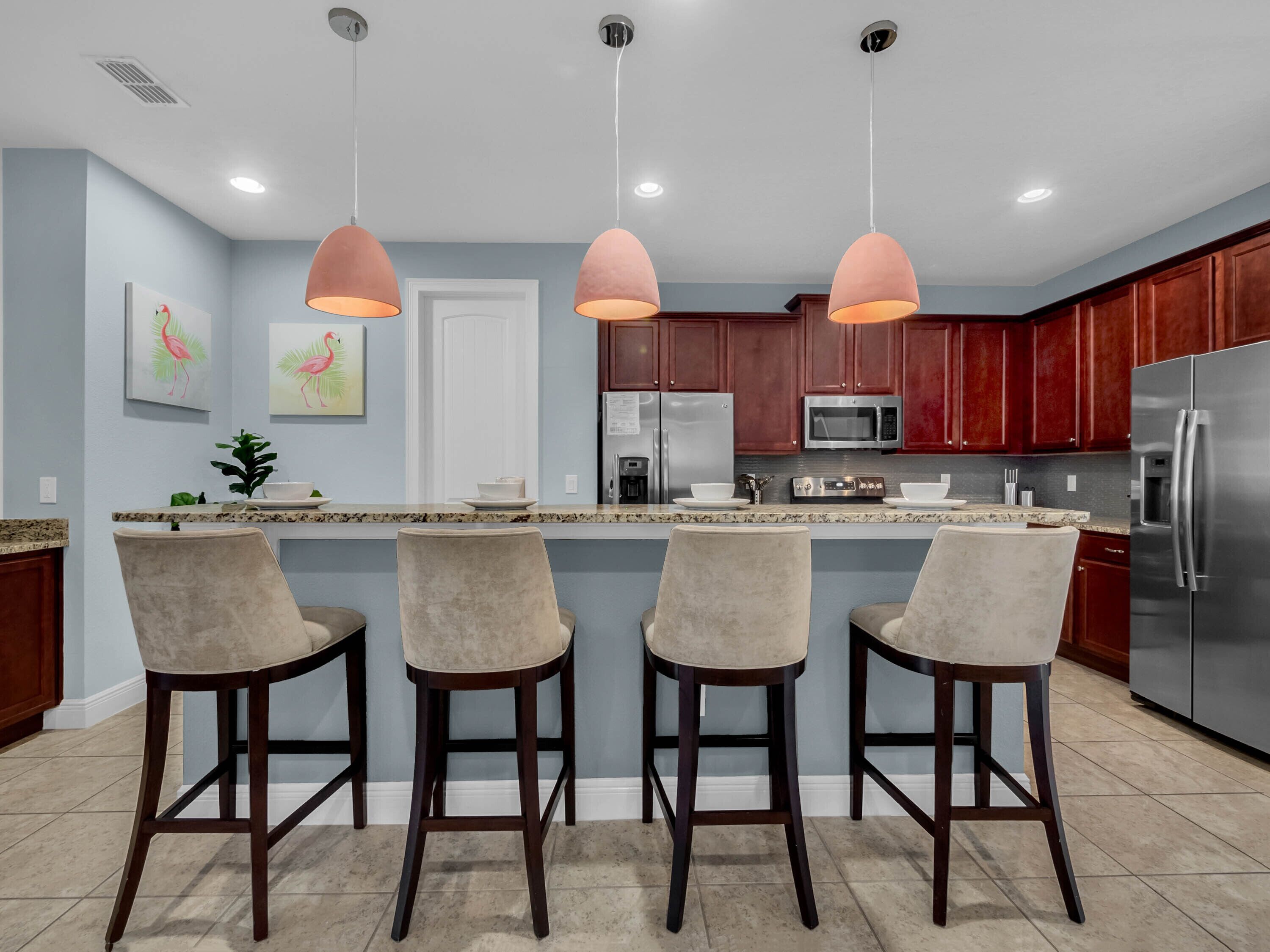 A modern kitchen with a central island, bar stools, stainless steel appliances, and pendant lighting.