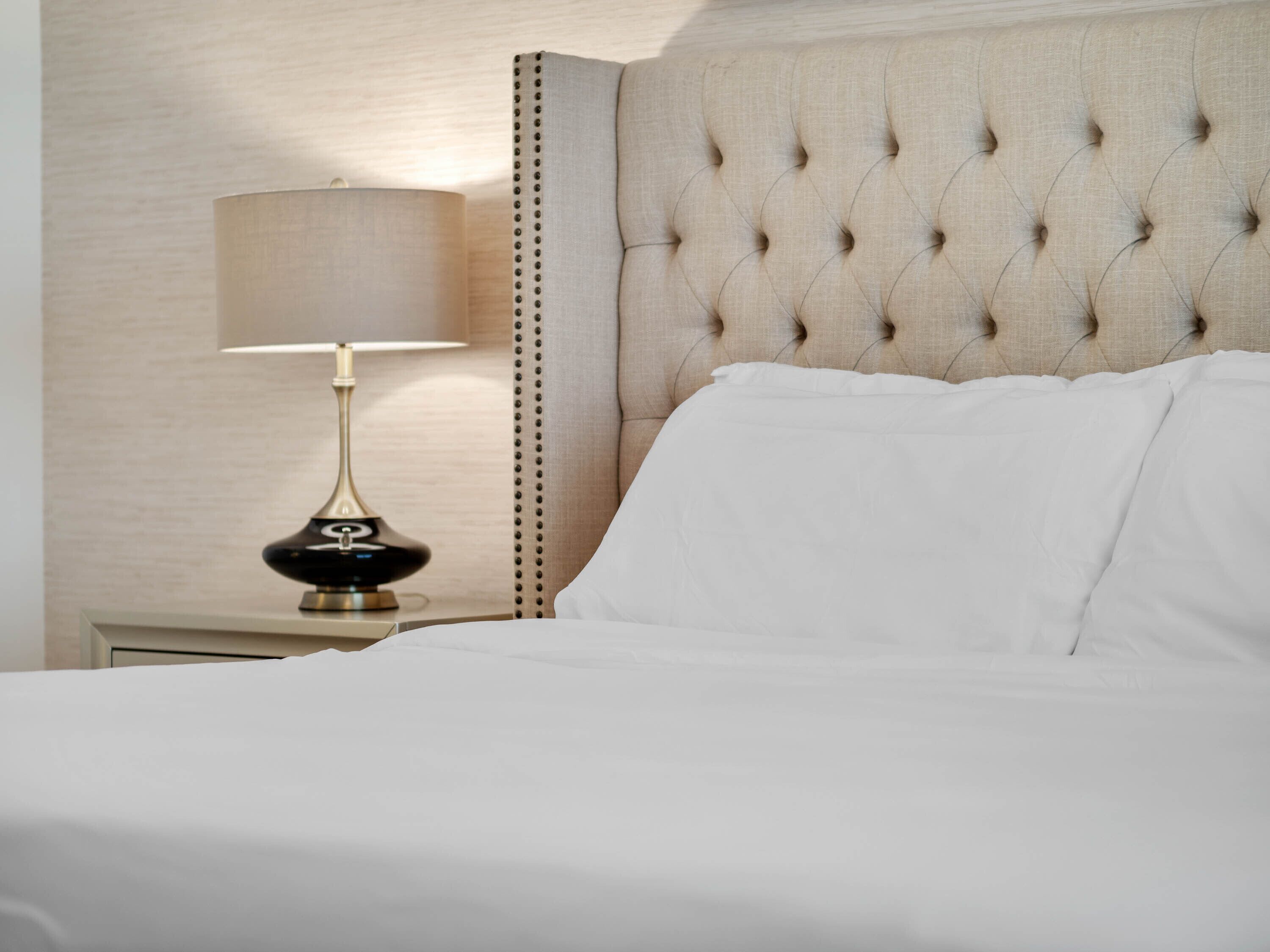 A neatly made bed with white linens, a tufted headboard, and a bedside lamp with a black base.