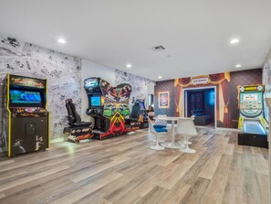 Ein Spielbereich mit Spielautomaten, einem weißen Tisch und blauen Stühlen.