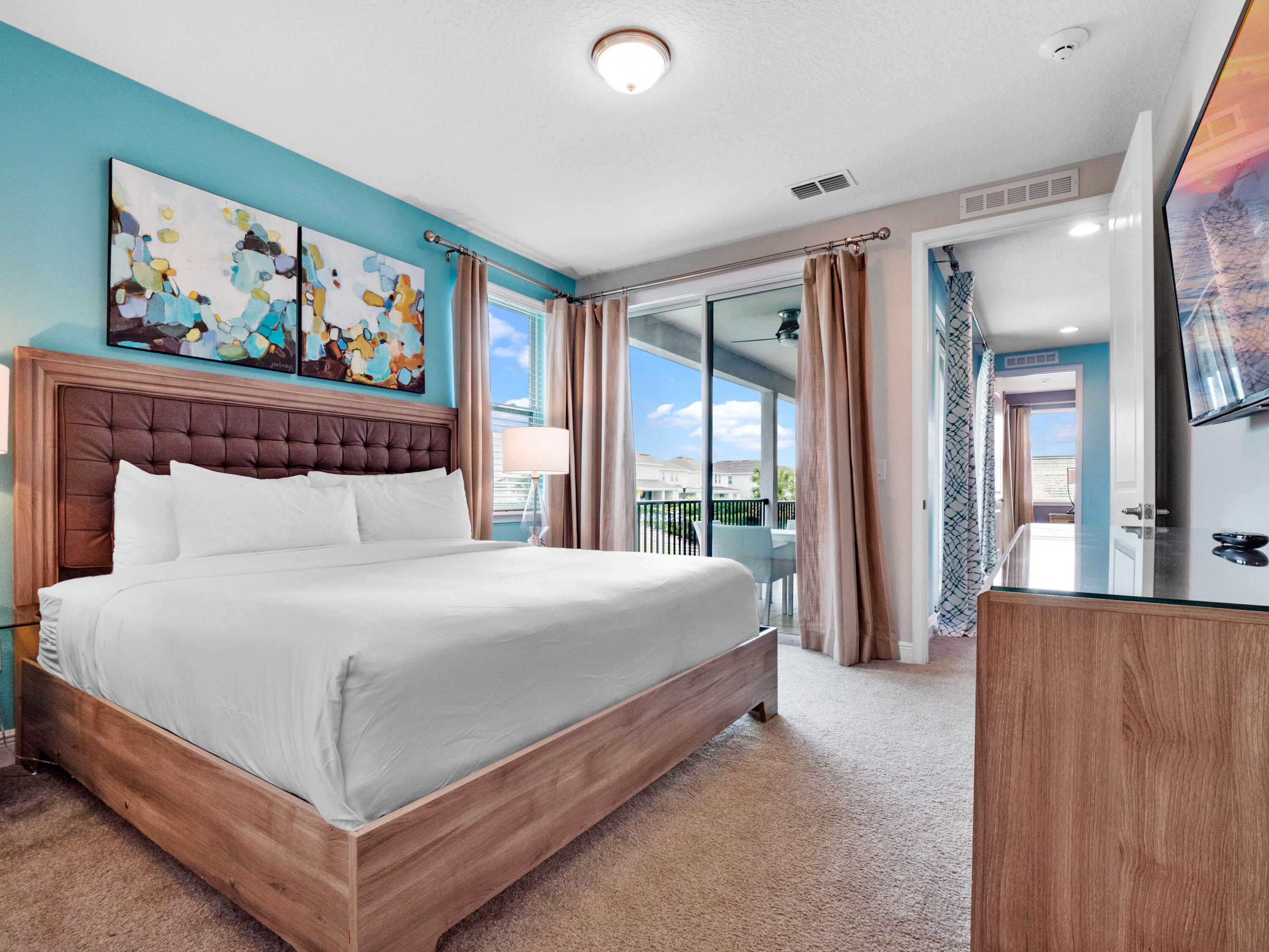 Habitación de hotel con una cama grande, cabecera de madera, televisor de pantalla plana, escritorio y balcón con vistas.
