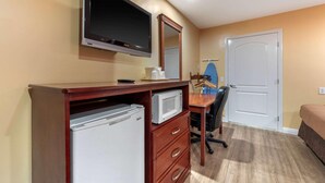 Habitación de hotel con escritorio de madera, televisor de pantalla plana, microondas, refrigerador, silla, cama y puerta.