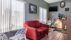 Una habitación con un sofá rojo, sillas blancas, televisor, reloj y cafetera.