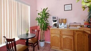 Un comedor con una mesa redonda, dos sillas, una planta en maceta, una cafetera y un armario.