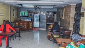 Un restaurant avec un sol carrelé, un téléviseur fixé au mur et un réfrigérateur rempli de boissons.