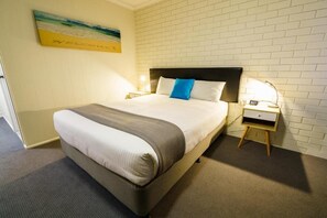 Een hotelkamer met een bed, nachtkastje, lamp en een schilderij aan de muur.