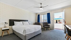 Une chambre d’hôtel équipée d’un lit, d’un bureau, de chaises, d’un ventilateur de plafond et d’une fenêtre avec des rideaux.
