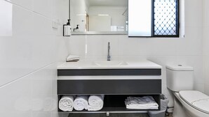 Une salle de bain moderne avec un lavabo blanc, un miroir et des toilettes.