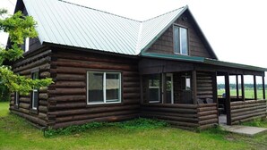 Une cabane en rondins avec un toit en métal, une véranda avec des sièges et une vue sur le paysage environnant.