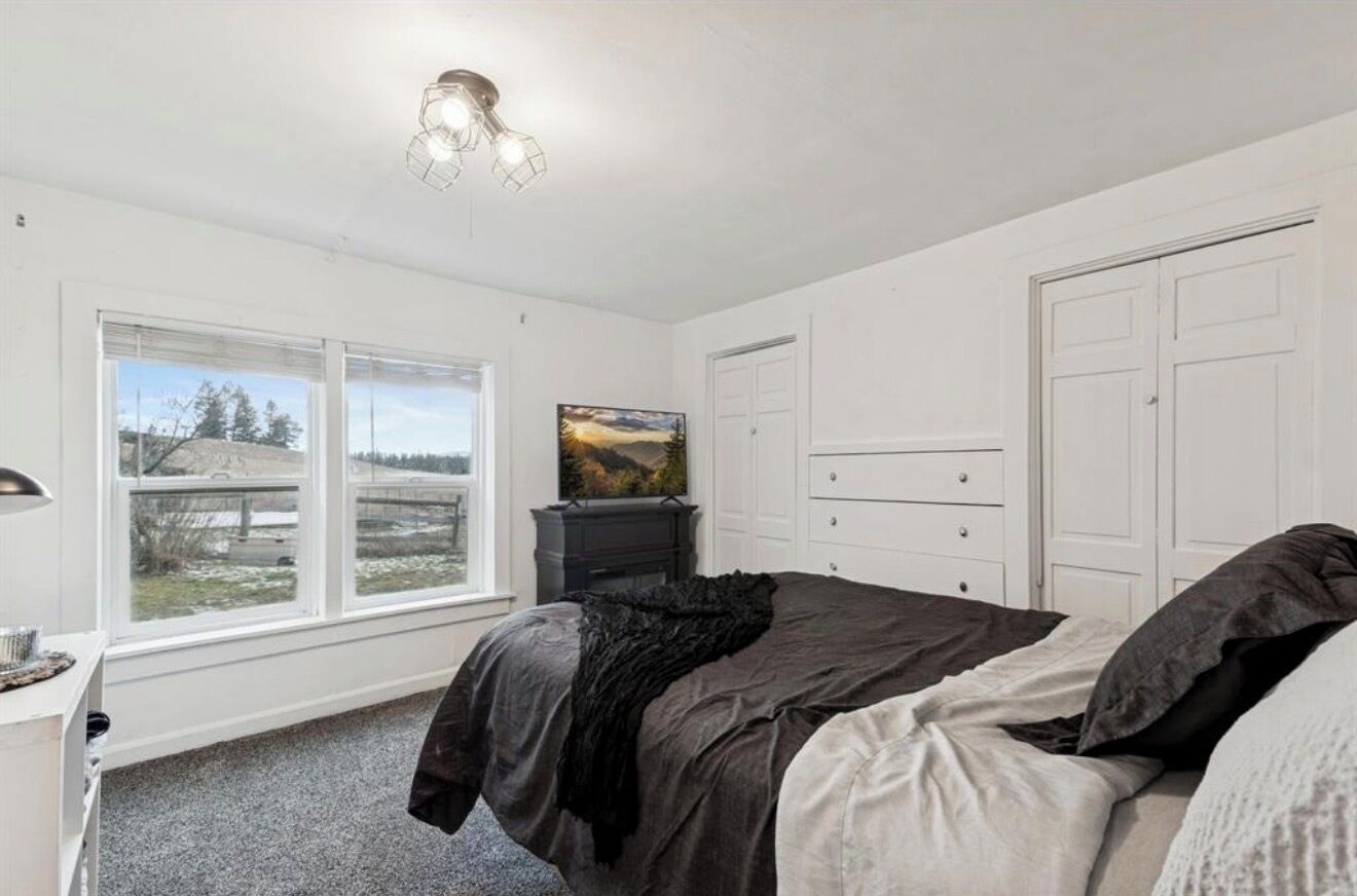 A bedroom with a bed, a dresser, a desk, a window with a view, and a painting on the wall.