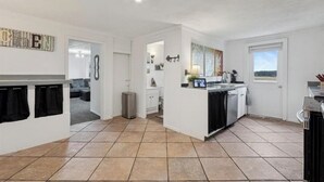 Une cuisine moderne avec des meubles blancs, un sol carrelé et une vue sur l’extérieur par une fenêtre.